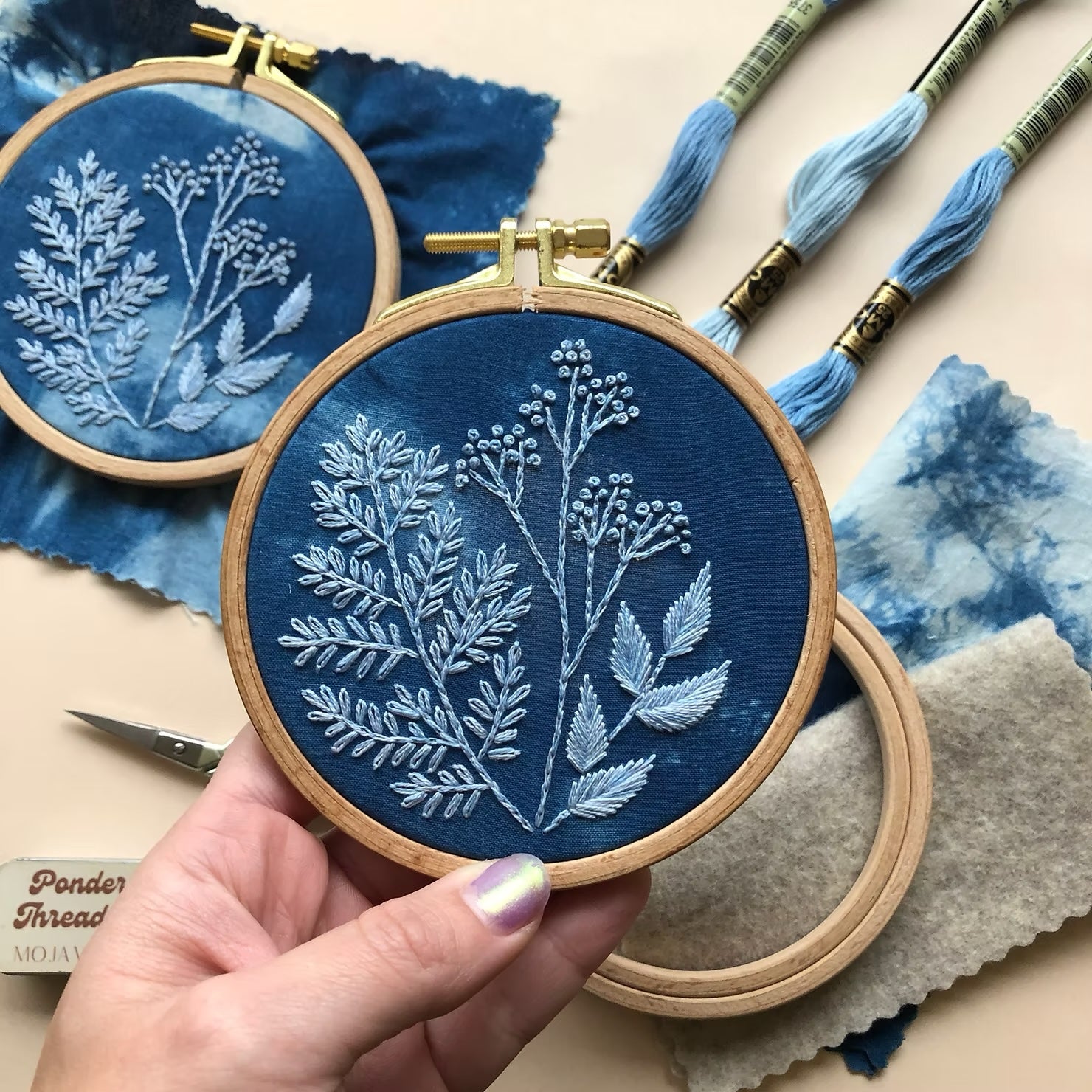 Hand holding an embroidery hoop with blue DMC floss stitching a design.